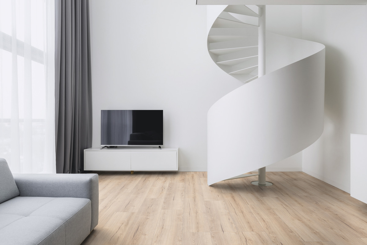 Hellbrauner Laminatboden mit sichtbarer Holzmaserung, integriert in eine moderne Wohnraumgestaltung mit weißer Wendeltreppe und grauem Sofa.